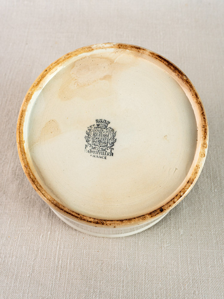 Antique French Badonviller rillettes pot underside, white ironstone with worn rim and Fabronnie France crest on light fabric.