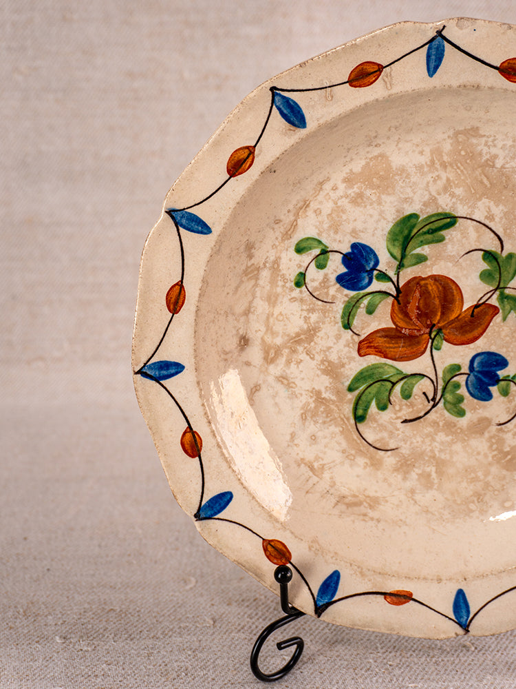 Antique French faience plate with scalloped edge and Normandy floral design, on cream, on metal stand.