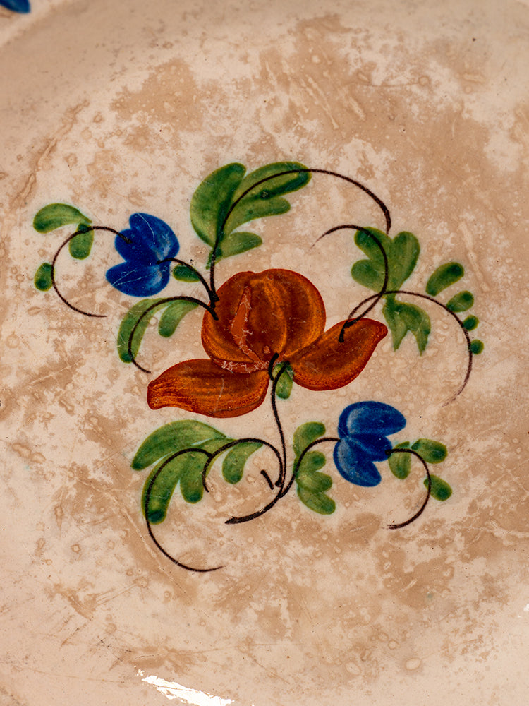 Antique French faience plate with hand-painted red-orange flower, blue blossoms, and green leaves on beige ceramic.