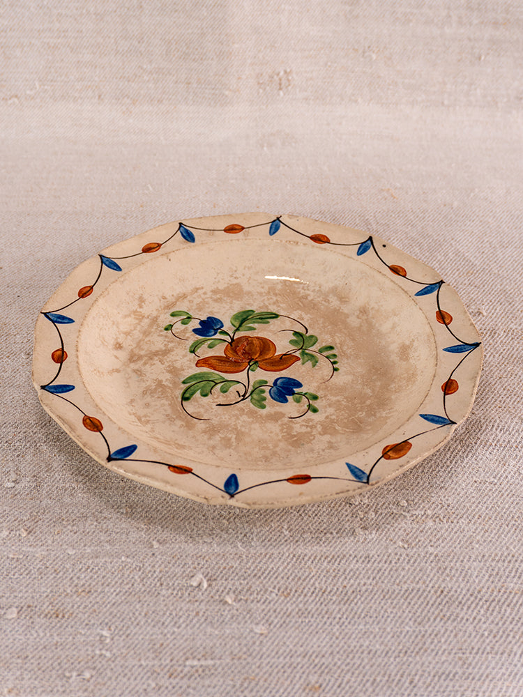 Early 19th-century French faience plate with orange and blue florals, blue leaf border; shown on light textured fabric.