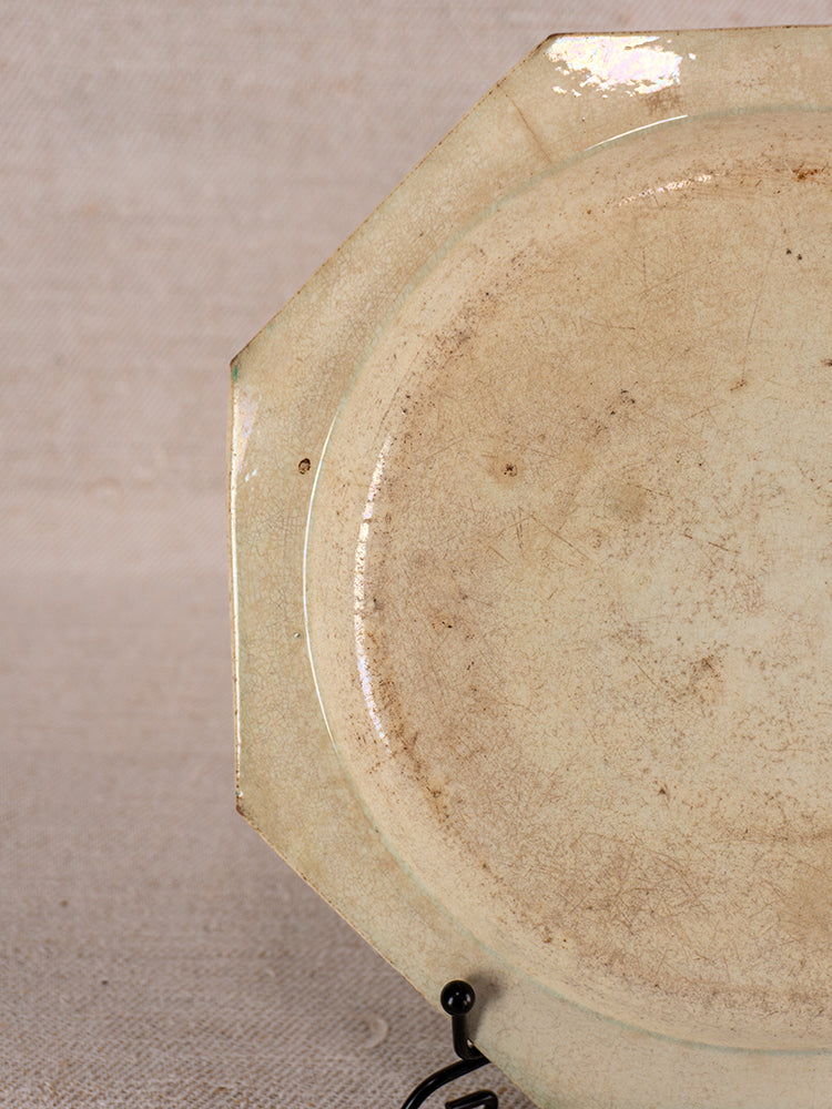 Antique French faience plate from Aumale, Normandy; octagonal, beaded rim, visible wear, on fabric background.