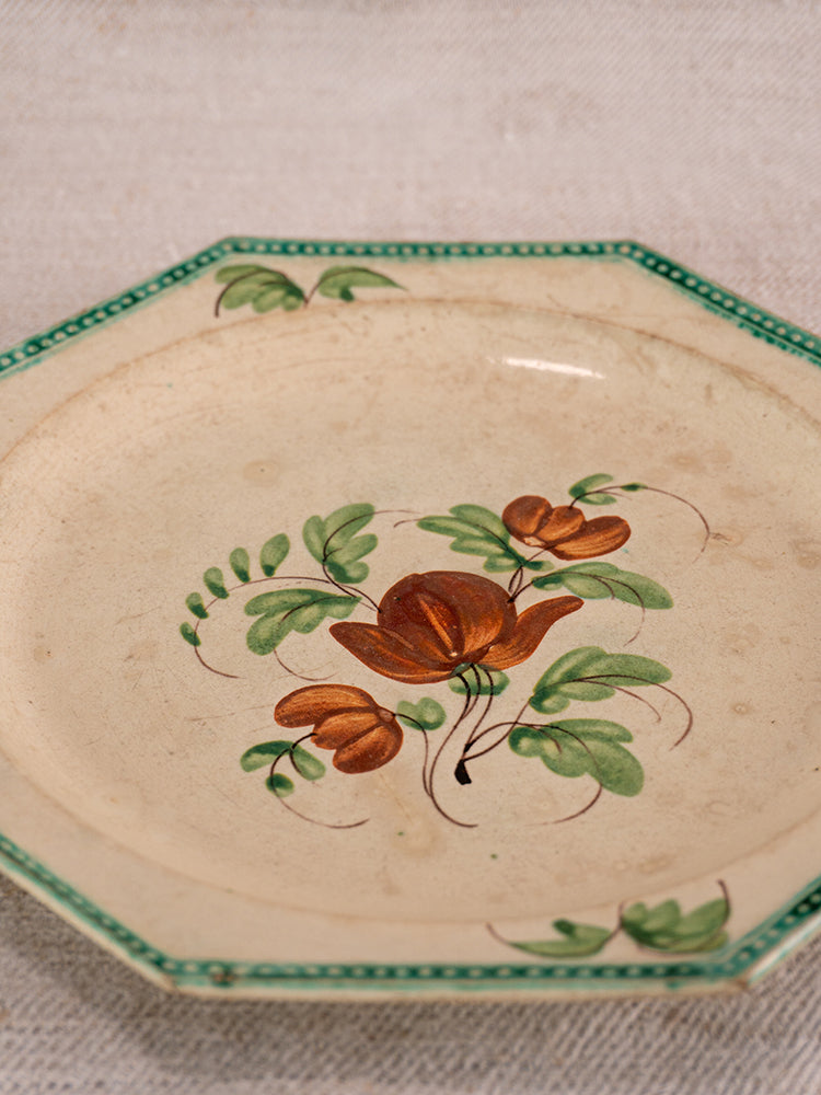 Antique French faience plate with beaded green rim and hand-painted orange floral motif on fabric background.