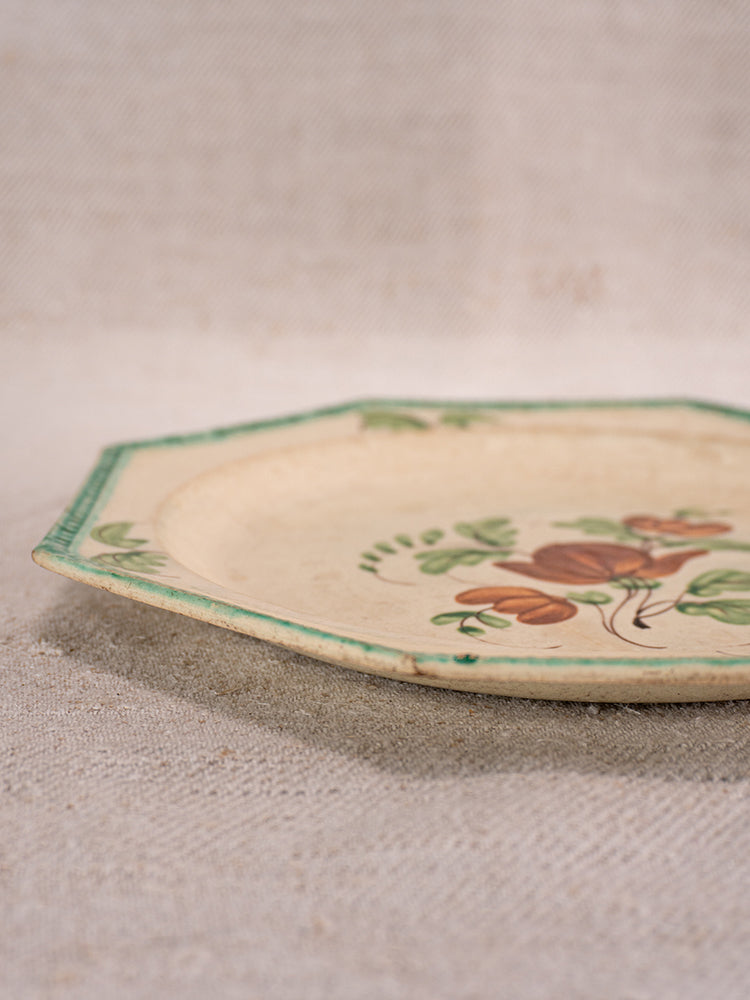 Octagonal French faience plate with beaded green rim and floral center on beige textured surface.
