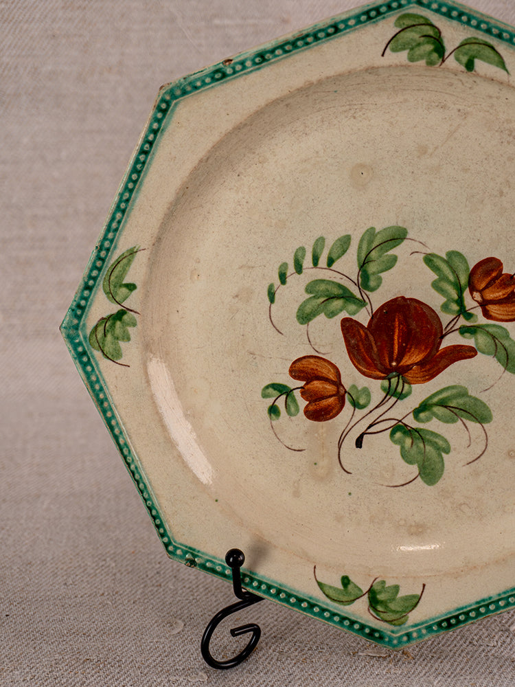 Antique French faience plate with octagonal shape, green border, and hand-painted flowers on stand.
