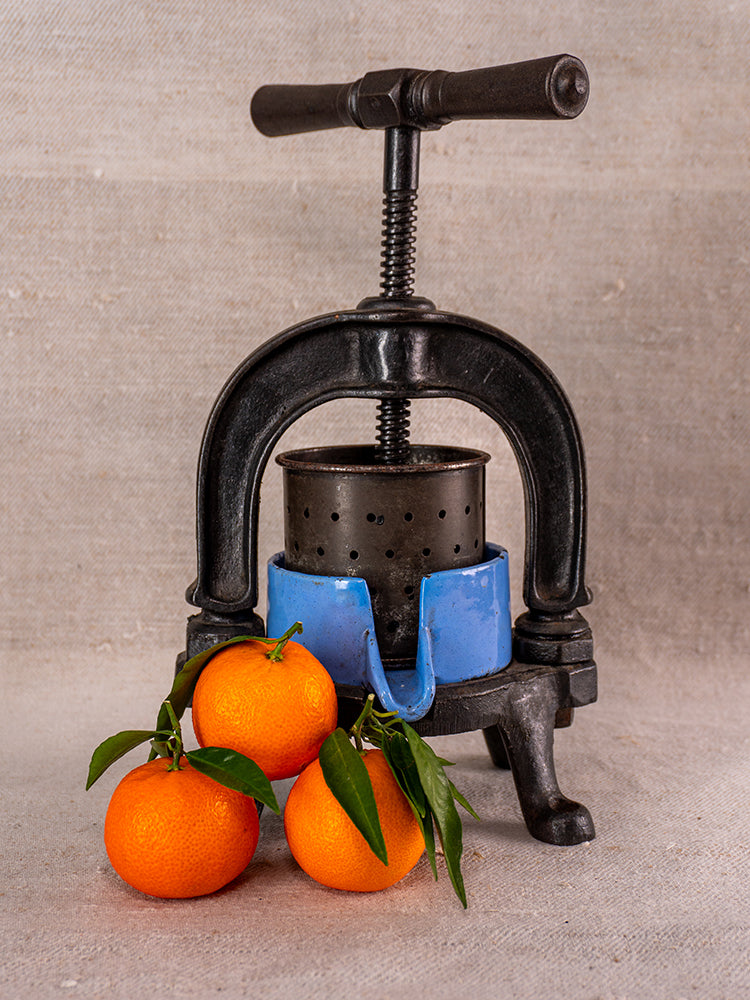 Antique French cast iron fruit press with blue enamel base and perforated metal cylinder on neutral fabric.
