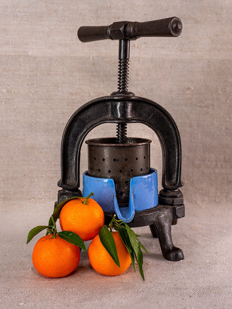 Antique French cast iron and blue enamel fruit press, c. 1900, with fresh oranges.