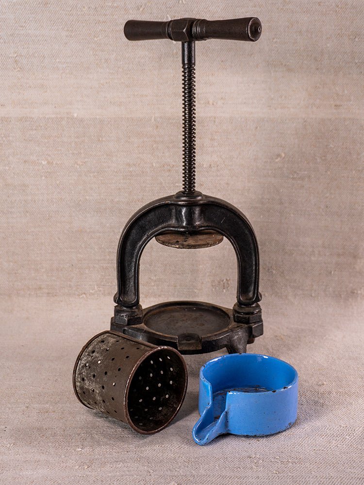 Antique French cast iron fruit press with blue enamel accents, circa 1900, on beige fabric.