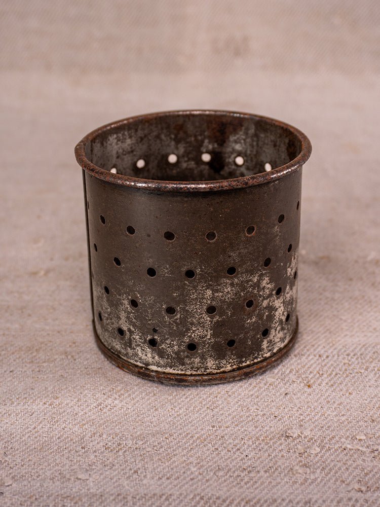 Antique French cast iron and blue enamel fruit press with aged patina on beige textured surface.