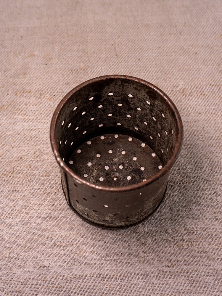 Antique French cast iron fruit press with blue enamel, gently worn, displayed on beige textured fabric.