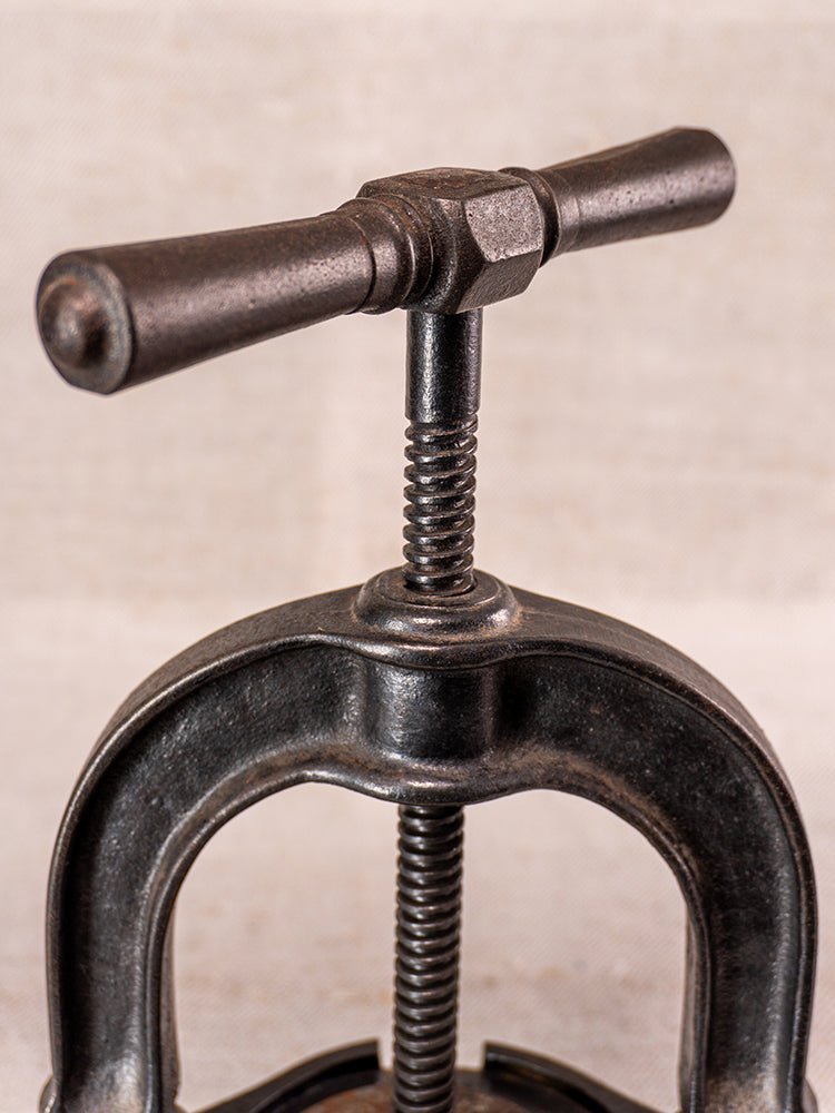 Antique French cast iron fruit press with blue enamel, T-handle and curved frame, on beige fabric.