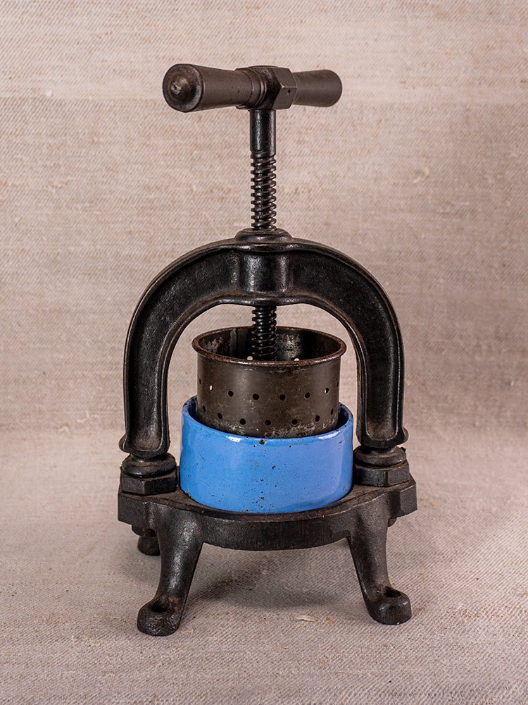 Antique French cast iron fruit press with blue enamel accents and screw handle on beige surface.