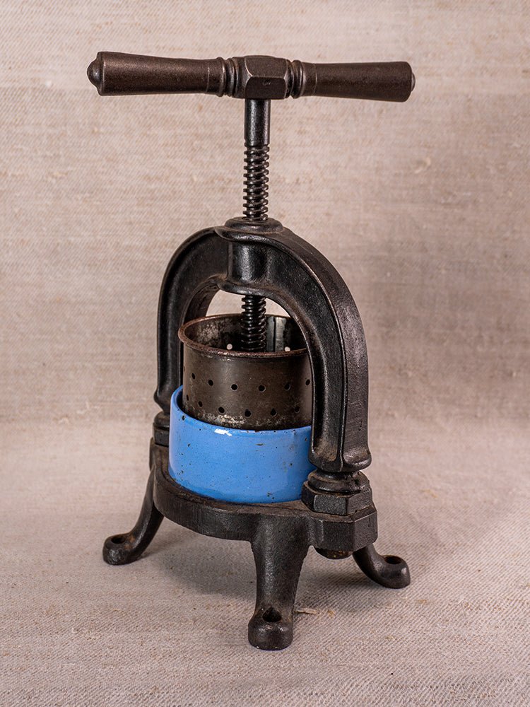 Antique French fruit press with black cast iron frame and blue enamel ring, on beige fabric.