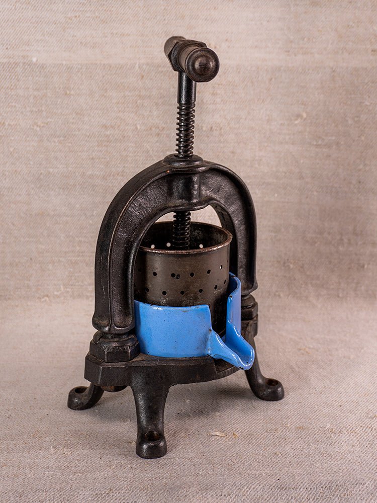 Antique French fruit press, c. 1900, cast iron and blue enamel, on textured fabric background.