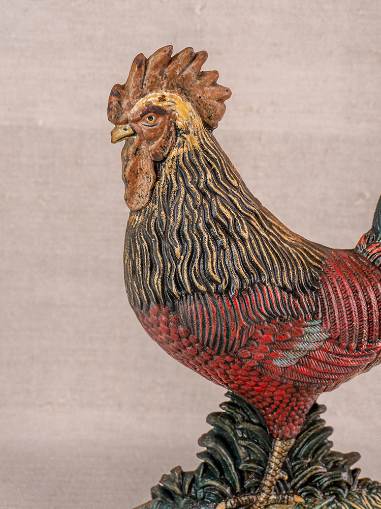 Antique French cast iron rooster doorstop with polychrome finish on neutral beige fabric background.