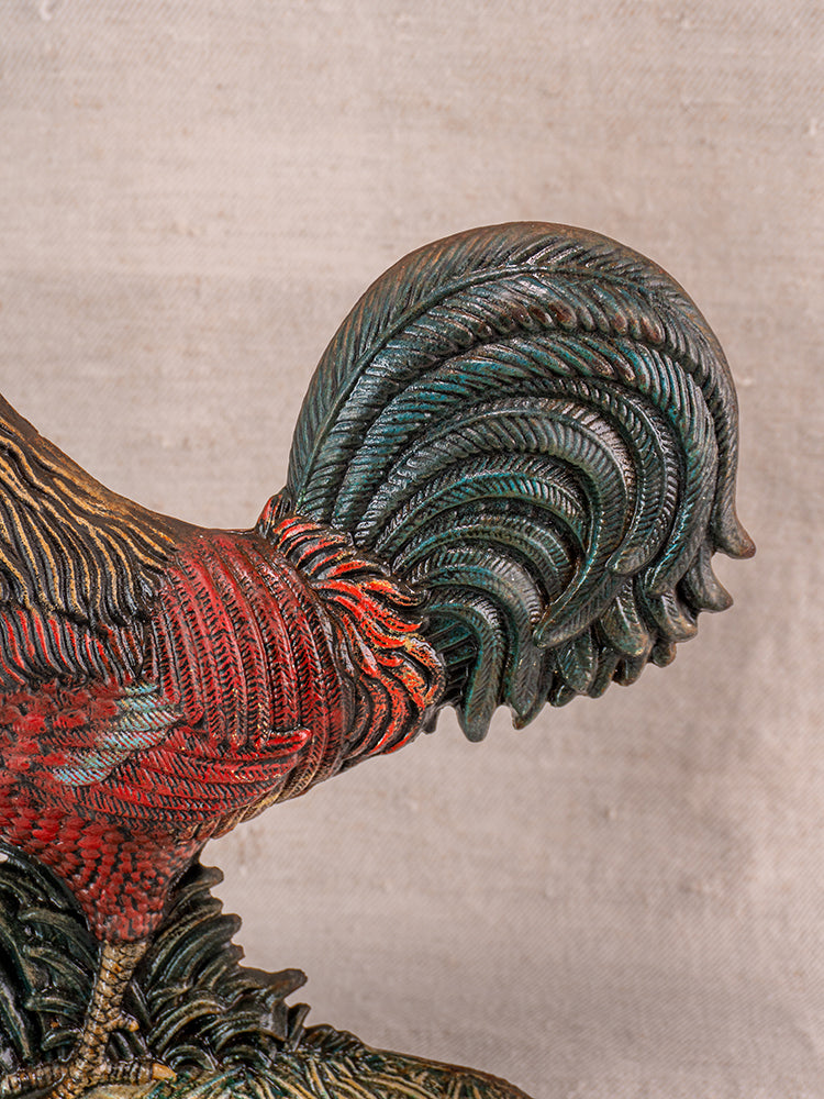 Antique French cast iron rooster doorstop with dark green tail and red-brown body, displayed on fabric.