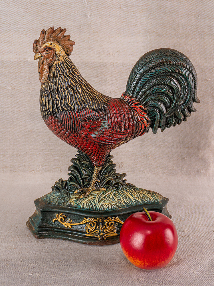Antique French cast iron rooster doorstop with polychrome finish on ornate base beside a red apple.