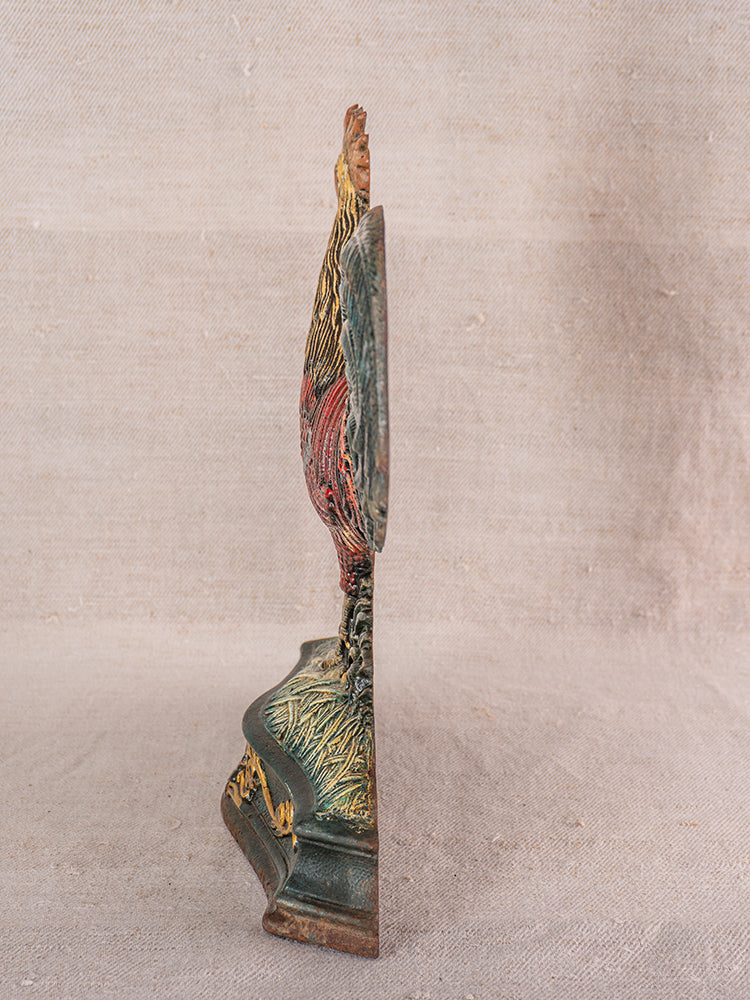 Antique French polychrome cast iron rooster doorstop with detailed feathers, decorative base on beige fabric background.