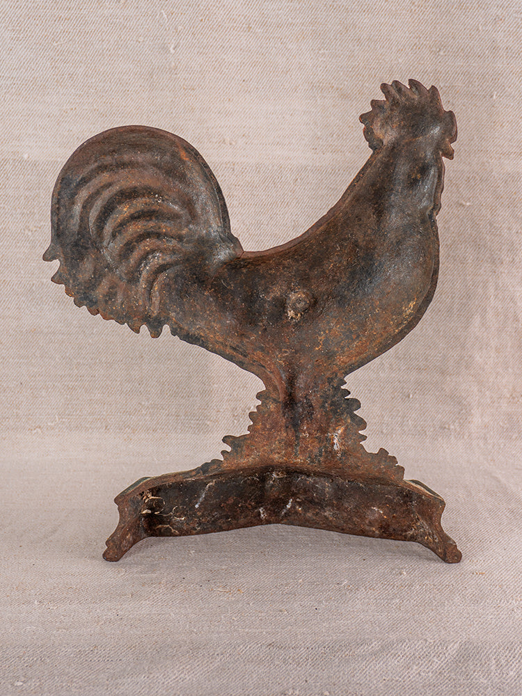 Antique French cast iron rooster doorstop with polychrome finish, detailed tail feathers on light textured fabric background.