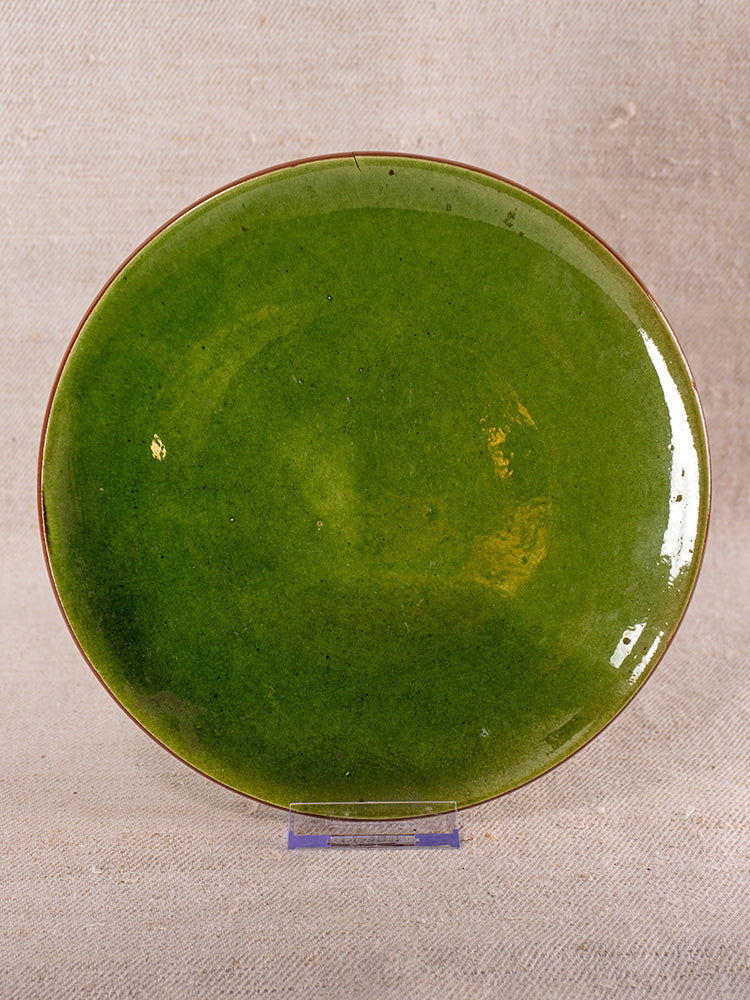 Mid-century French green glazed earthenware berry drainer displayed upright on clear stand with beige textured fabric backdrop.