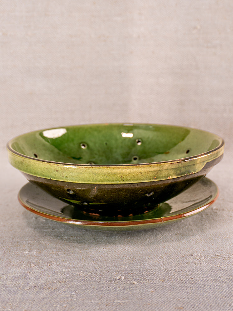 Antique French green glazed earthenware berry drainer set with saucer, mid-20th century, on neutral textured background.