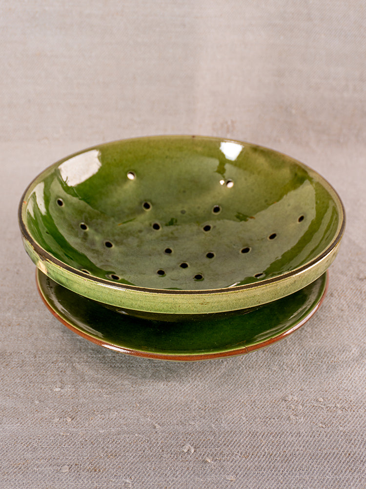 Antique French green glazed earthenware berry drainer set with matching plate, shown on a textured beige surface.
