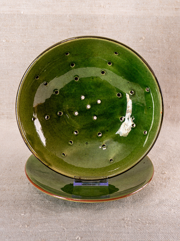 Antique French green glazed earthenware berry drainer set on matching plate, neutral fabric background, mid 20th century.