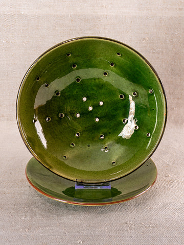 Antique French green glazed earthenware berry drainer set on matching plate, neutral fabric background, mid 20th century.