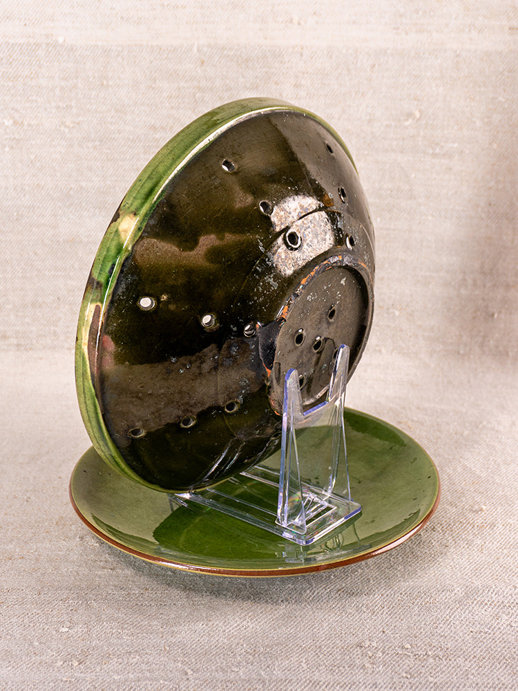 Antique French green glazed earthenware berry drainer set with plate and colander on clear stand, beige fabric backdrop.