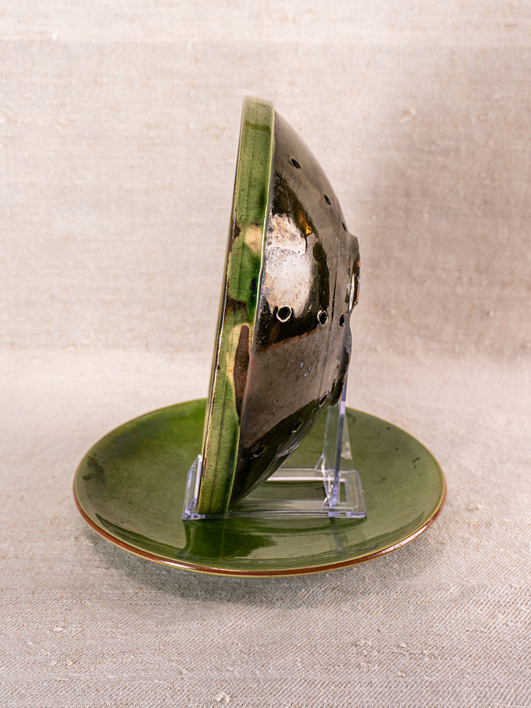 Mid-century French green glazed earthenware berry drainer set with glossy plate and pierced bowl on clear stand, beige backdrop.