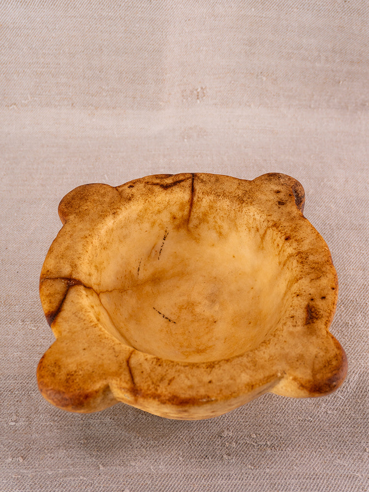 Antique French marble mortar and pestle, 18th-century Provençal origin, yellow marbled patina, on beige textured surface.