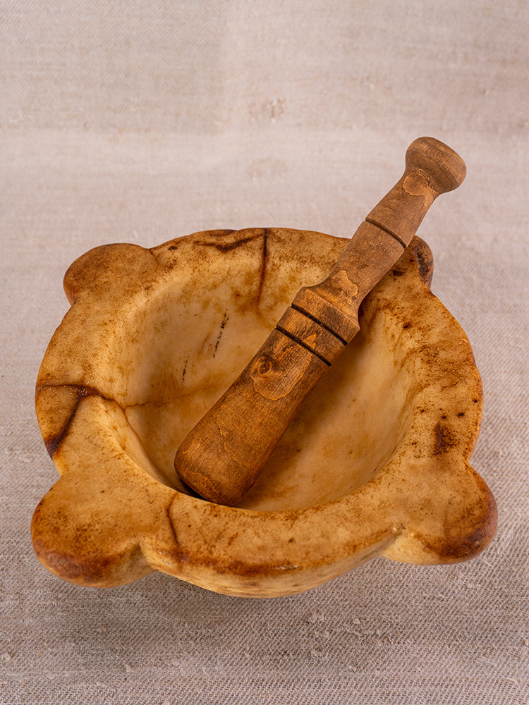 Antique French marble mortar and pestle with 18th-century Provencal form on textured beige fabric background.