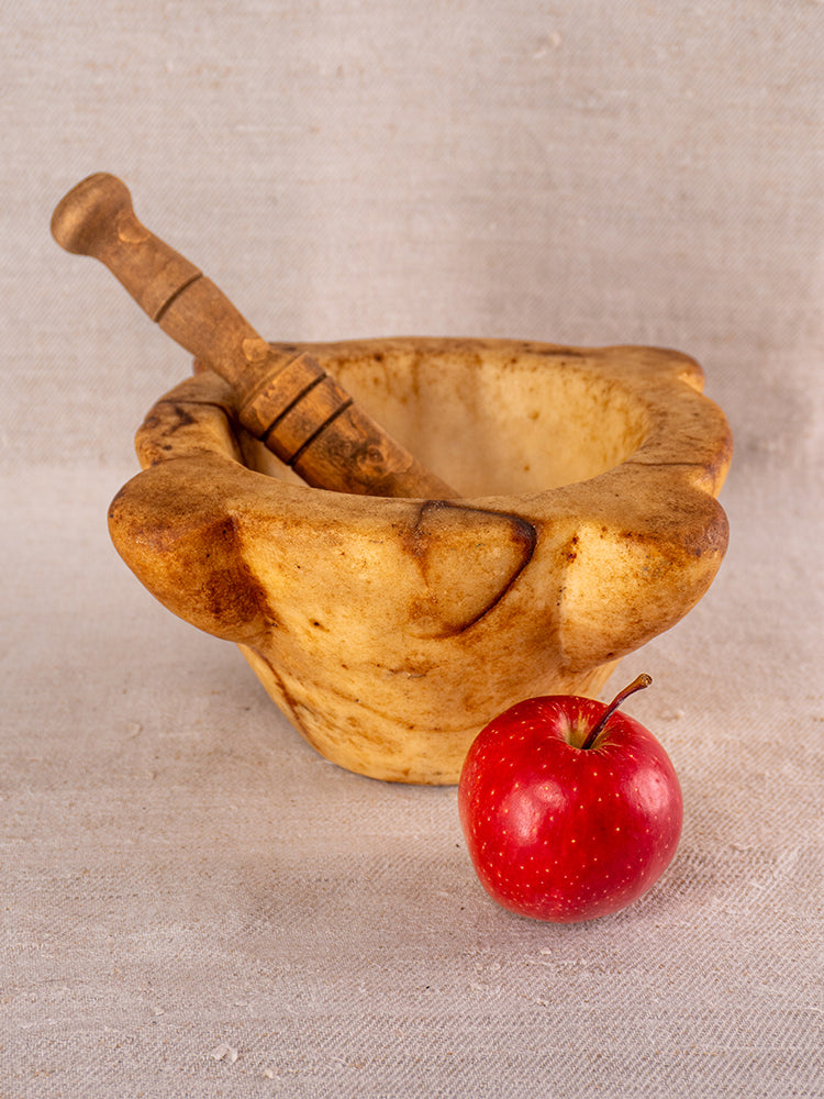 Antique French marble mortar and pestle with Provencal silhouette on beige fabric, red apple in foreground.