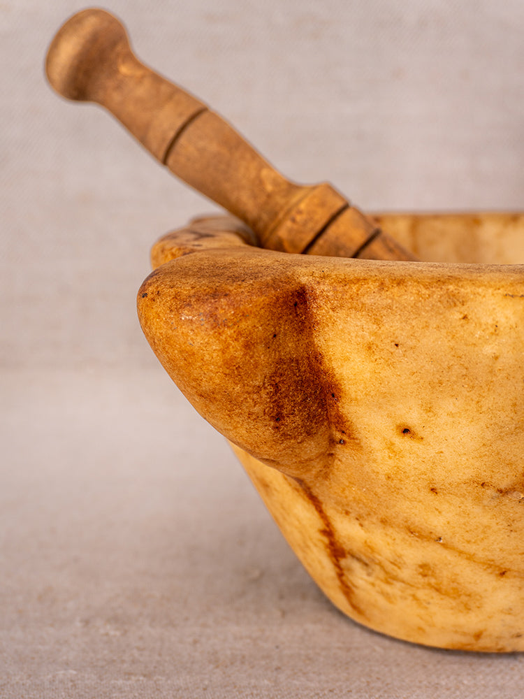 Antique French marble mortar with yellowish bowl and wooden pestle, Provencal silhouette on textured backdrop.