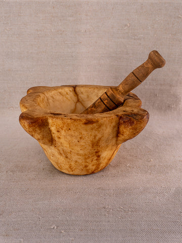 Antique French marble mortar and pestle with Provencal silhouette on textured beige fabric, showcasing aged patina.