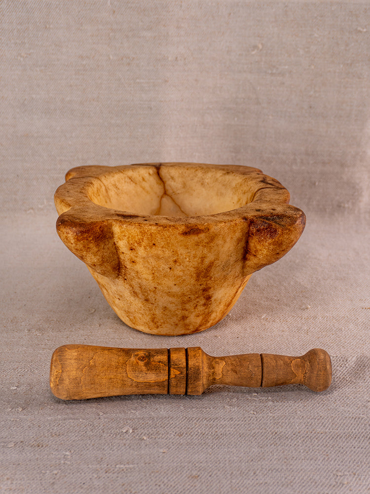 Antique French marble mortar and pestle with rustic brown tones on neutral textured fabric background.