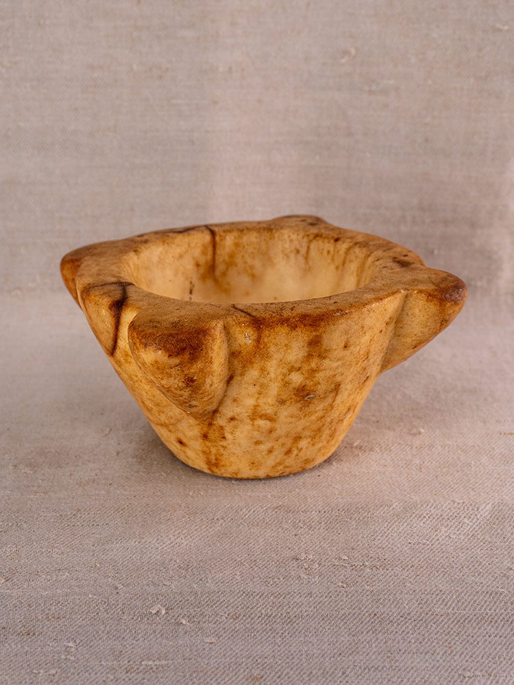 Antique French marble mortar and pestle with Provencal lines and textured surface on a neutral fabric backdrop.