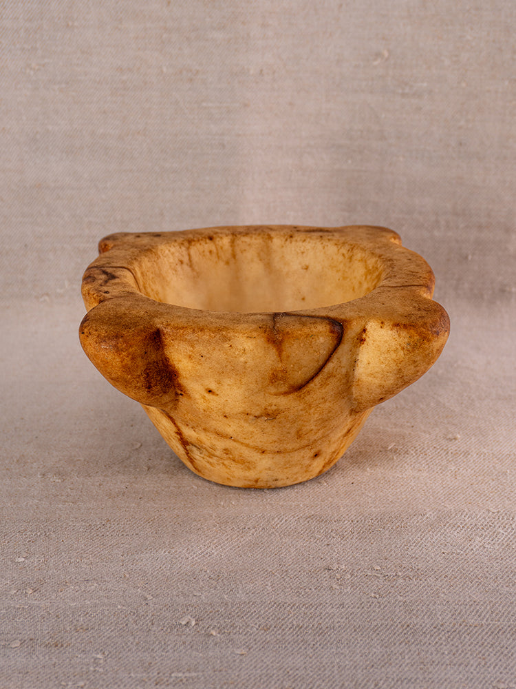Antique French marble mortar and pestle with Provençal silhouette, light brown marbling, on textured beige fabric.