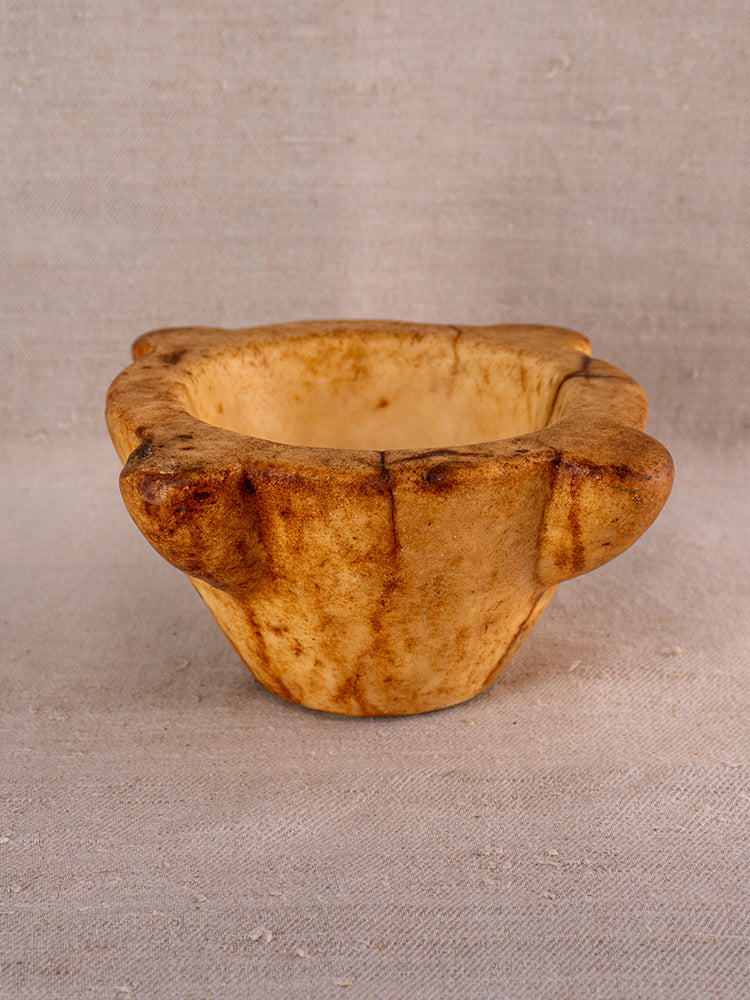 Antique French marble mortar and pestle with Provencal silhouette, thick tan edges on a beige surface, evoking rustic 18th-century charm.