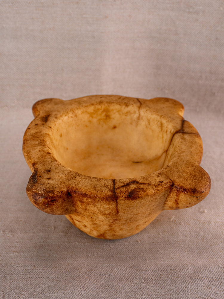 Antique French marble mortar and pestle with four rounded lobes on textured beige fabric, Provencal kitchen style.