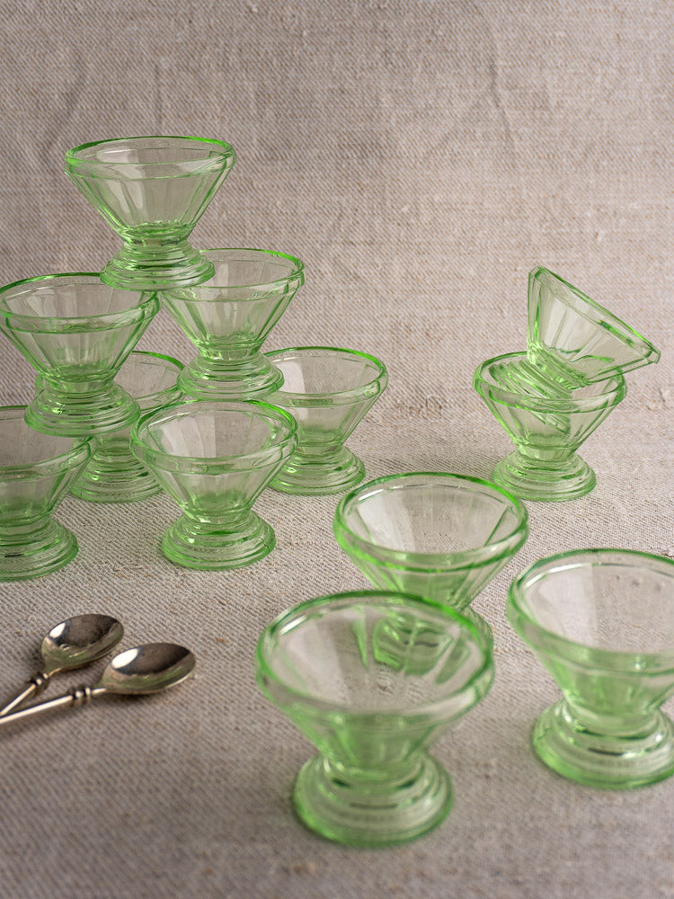 Set of 12 Antique French uranium glass Art Deco sherbet coupes on neutral fabric with two silver spoons.