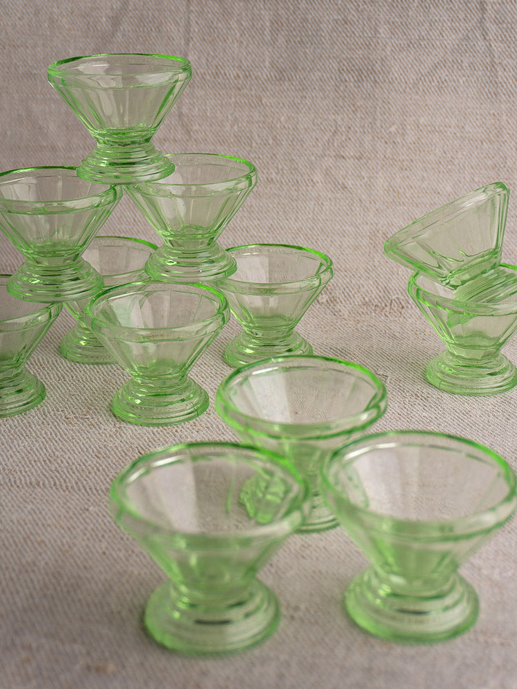 Set of twelve antique French uranium glass sherbet coupes arranged playfully on a textured beige surface.