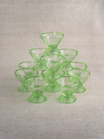 Set of 12 antique French uranium glass sherbet coupes, Art Deco, arranged on neutral textured fabric.