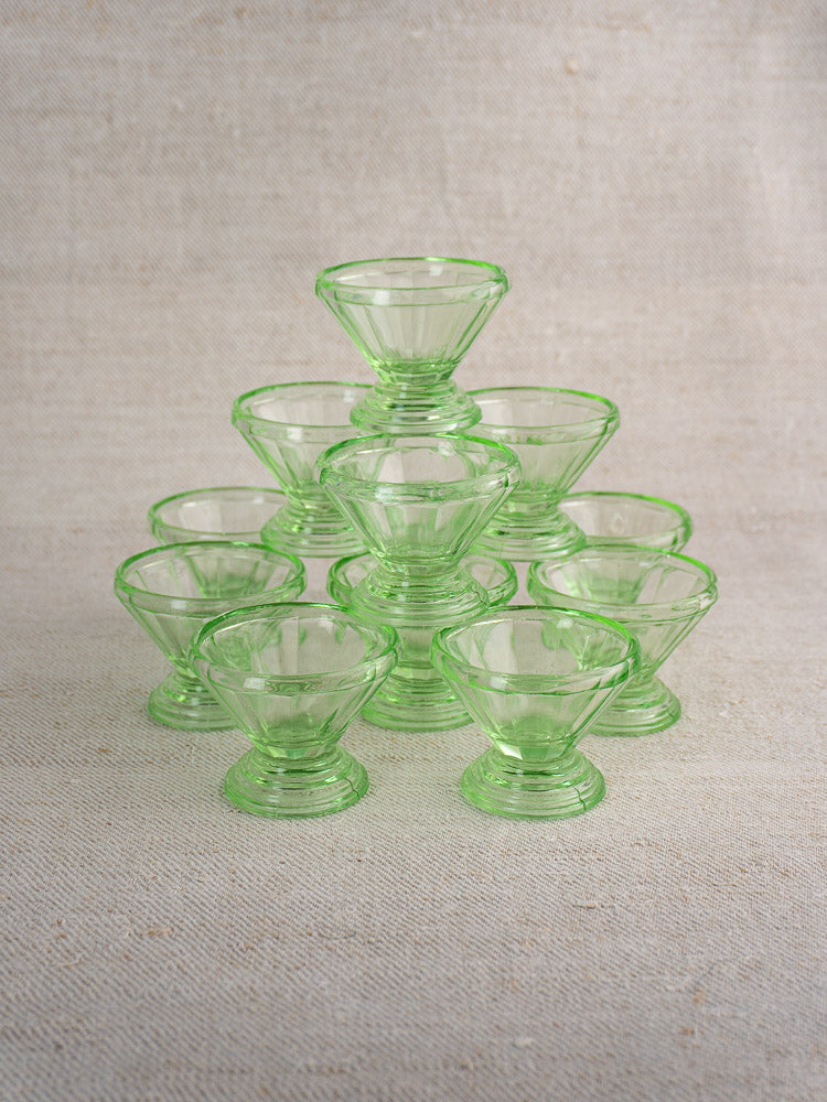 Set of 12 antique French uranium glass sherbet coupes, Art Deco, arranged on neutral textured fabric.