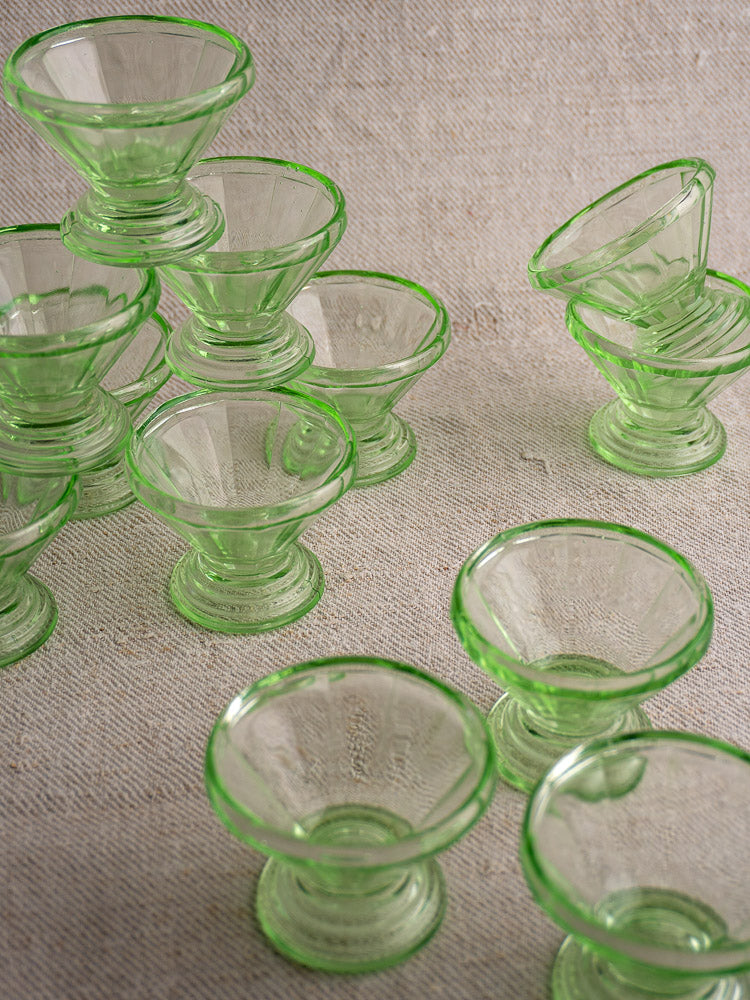 Antique French uranium glass sherbet coupes in Art Deco style, grouped and stacked on a textured beige surface.