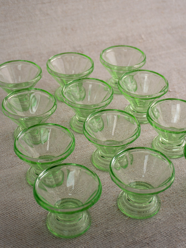 Set of 12 antique French uranium glass sherbet coupes with Art Deco wide tops, on textured beige surface.