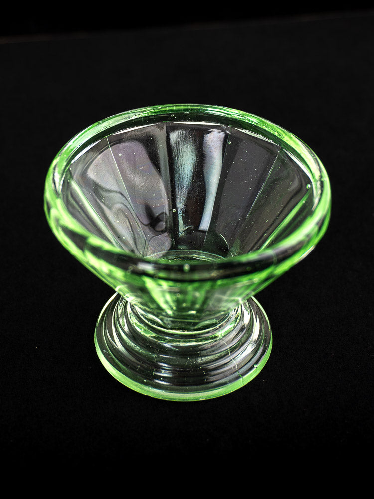Green uranium glass Art Deco sherbet coupe with flared bowl and pedestal base on black surface.