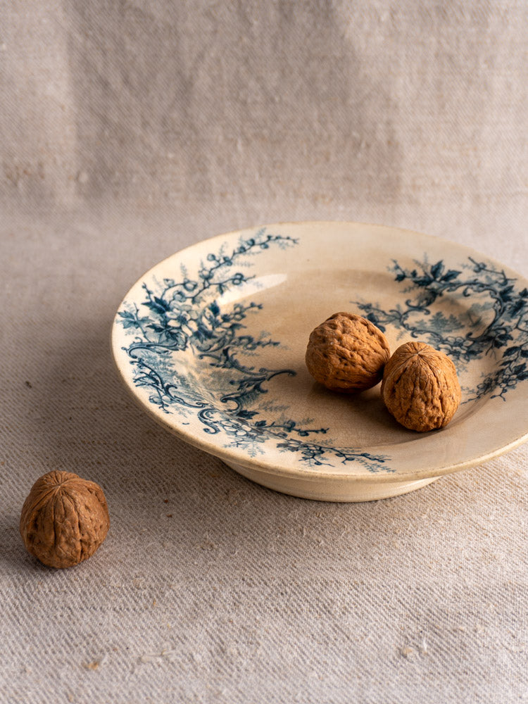 Antique French compote plate by Boulenger Choisy-le-Roi, Pompadour pattern, blue floral on beige ceramic, on textured fabric.