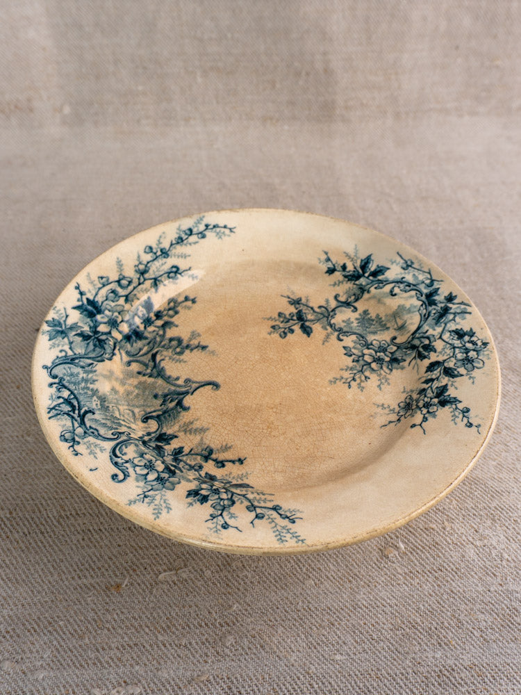 Antique French compote plate by Boulenger Choisy-le-Roi, Pompadour pattern, blue floral rim, age wear on beige textured fabric.