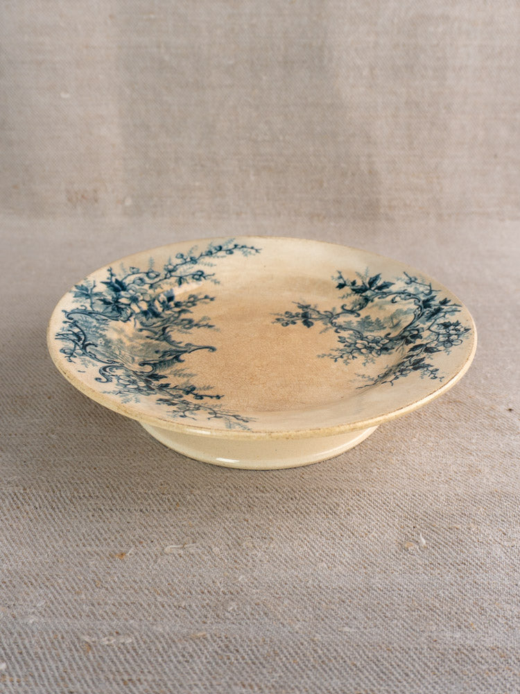 Antique French compote plate by Boulenger Choisy-le-Roi, Pompadour pattern, blue floral on beige ceramic, on textured fabric.