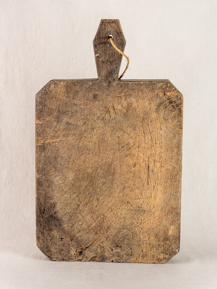 Antique French cutting board, hand carved with diamond handle, vintage wood patina and unique marks, upright on light background.